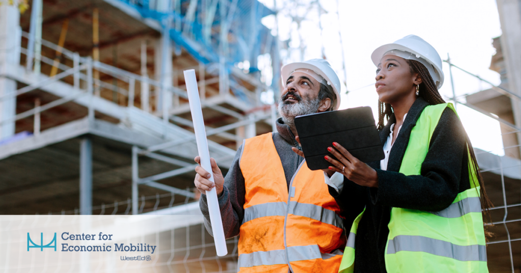 Two construction workers wearing hard hats and safety vests stand at a building site, reviewing a tablet and holding rolled plans, with scaffolding in the background and the WestEd Center for Economic Mobility logo in the corner.